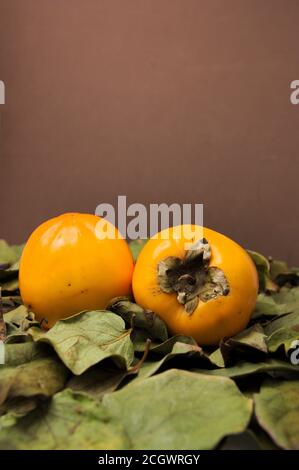 Close-up of a pair of ripe persimmons that are on some dry leaves. Brown background with copy space Stock Photo