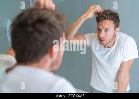 Hair loss man looking in bathroom mirror styling hairstyle with gel or checking for hair loss or grey hairs. Unhappy male health problem Stock Photo