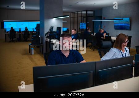 Group of Security data center operators (administrators) working in a group at a CCTV monitoring room while looking at multiple monitors ( computer sc Stock Photo