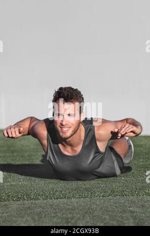 Lower back exercises for strengthening the muscles for spine health. Fitness man doing superman exercise workout with arms raised on gym floor Stock Photo