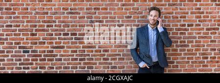 Business man talking on mobile phone panoramic banner of brick wall background texture. Happy young businessman using cellphone in urban setting Stock Photo