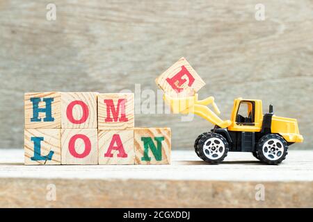 Toy bulldozer hold letter block e to complete word home loan to on wood background Stock Photo