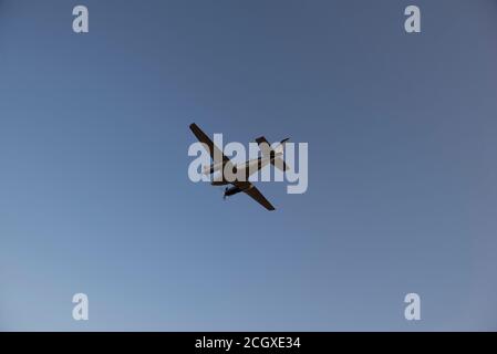 Bottom view of propeller-powered airplane taking off from the airport during sunset. Airplane silhouette in the clear sky. Stock Photo