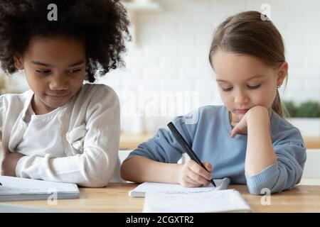 Focused little multiracial sisters preparing homework indoors. Stock Photo