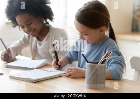 Small multiracial children enjoying preparing homework indoors. Stock Photo
