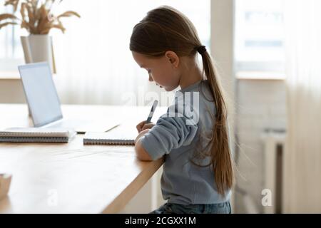Focused small adorable caucasian girl preparing homework alone. Stock Photo