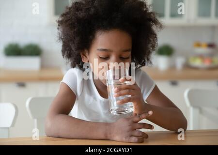 Thirsty small curly african american little child girl drinking water. Stock Photo