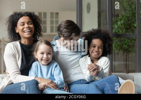 Laughing multiracial couple enjoying watching television funny films with kids. Stock Photo