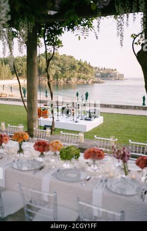 A wedding table decorated with bouquets of flowers overlooking the stage for the performance of musicians against the backdrop of water, trees and Stock Photo
