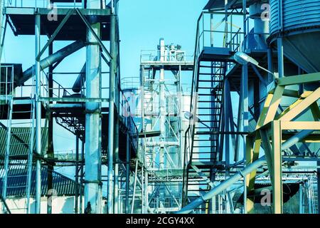 Agricultural Silos. Building Exterior. Storage and drying of grains, wheat, corn, soy, sunflower. Metal stairs and structures. Blue sky background Stock Photo