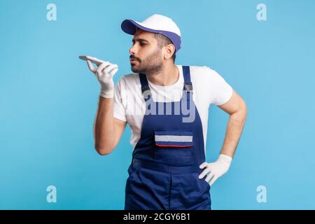 Virtual assistant. Handyman in overalls and gloves talking to phone recording message, using digital voice app to accept online order as delivery, rep Stock Photo
