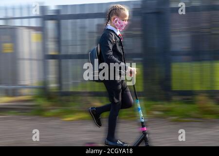 A ten year old schoolgirl in school uniform scooting along wearing a face mask. Stock Photo