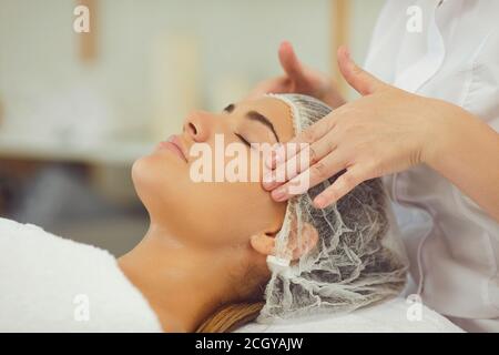 Hands of therapist making lifting facial massage for relaxing young woman Stock Photo