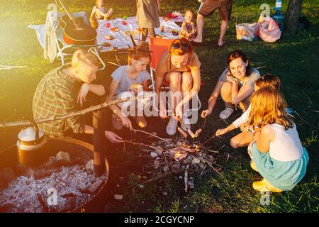 People sitting in a tight circle around bonfire, cooking sausages Stock Photo