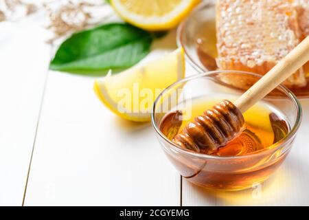 Honey with wooden honey dipper in bowl with sliced lemon on white wood background. Stock Photo