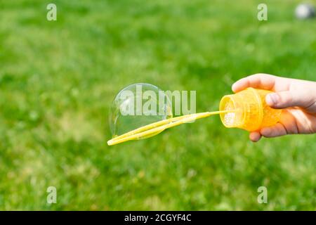 childs hand holding a wand for blowing soap bubbles against green grass in a sunny summer day Stock Photo