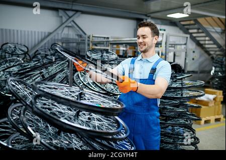 Mechanic in uniform holds bicycle wheel on factory Stock Photo