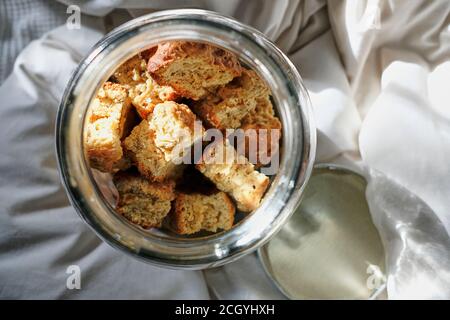 Freshly baked rusks inside a glass container on bedding and white linen. Stock Photo
