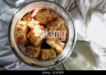 Freshly baked rusks inside a glass container on bedding and white linen. Stock Photo