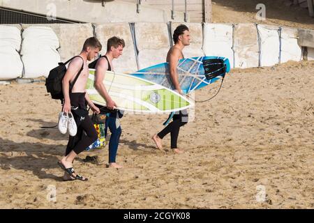 Three surfers carrying their surfboards and walking across Fistral Beach in Newquay in Cornwall. Stock Photo