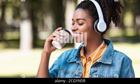 Happy Black Woman Enjoying Coffee And Music Walking In Park Stock Photo