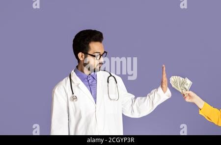 Reducing bribery and corruption. Honest Indian doctor refusing to take money from patient on violet background Stock Photo