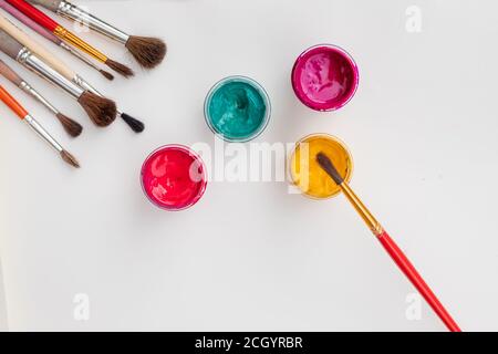 Open gouache jars on white background, flat lay composition,top view.Copy space.Flat lay composition with gouache colors and paintbrushes.advertising Stock Photo