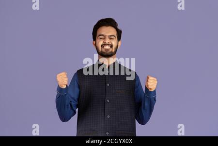Triumphant Indian man making YES gesture, celebrating his success on violet background Stock Photo