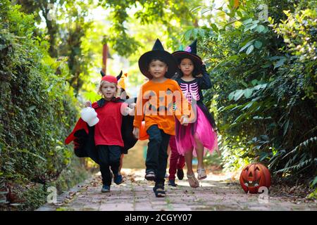 Child in Halloween costume. Mixed race Asian and Caucasian kids trick or treat on suburban street. Little boy and girl with pumpkin lantern and candy Stock Photo