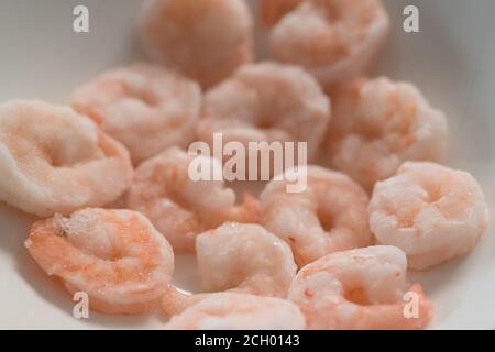 Frozen pre cooked shrimps in white bowl, shallow focus Stock Photo