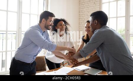 Overjoyed multicultural coworkers stack hands engaged in teambuilding Stock Photo