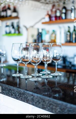 Collection of wine glasses on a bar's counter with bottles behind Stock Photo