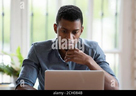 Pensive biracial male employee work on laptop thinking Stock Photo