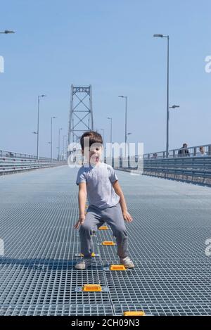 Isolated. Boy jumping with arms and legs open. Happy little boy disheveled jumping on bridge background. The concept of a happy childhood, sports and Stock Photo