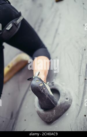Low angle close up view of rock climber female foott on grey artificial climbing wall. Stock Photo