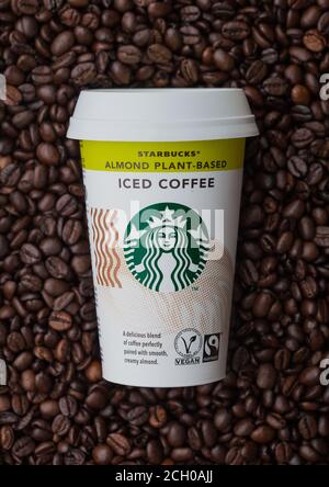 LONDON, UK - SEPTEMBER 09, 2020: Paper cup of Starbucks Almond plant based iced cold coffee on top of fresh raw coffee beans. Stock Photo