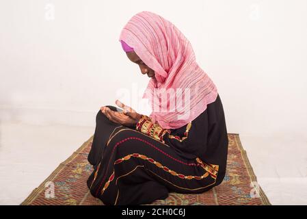 portrait of muslim woman praying alone sitting on a tablecloth, indoors Stock Photo
