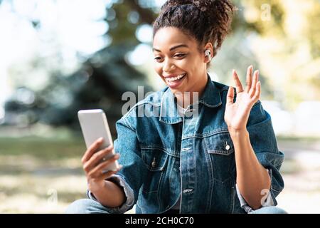 Black Woman With Smartphone Making Video Call Sitting In Park Stock Photo