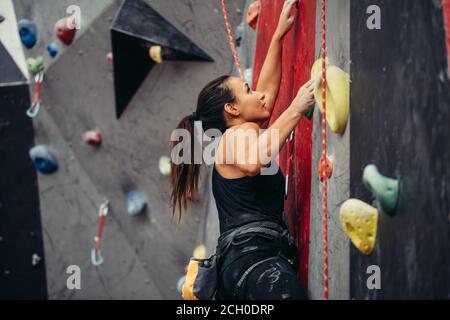 Extreme sport, stress relief, bouldering, people and healthy lifestyle concept. Young sporty muscular woman climbing up on top of rock wall in gym, si Stock Photo