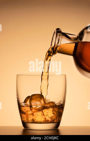 alcoholic drink, poured from a glass from a bottle on an orange gold background. whiskey, cognac or Bourbon Scotch Stock Photo
