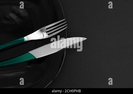Empty black slate plate, cutlery on dark stone table and napkin. Food background for menu, recipe. Table setting. Flatlay, top view. Concept modern sh Stock Photo