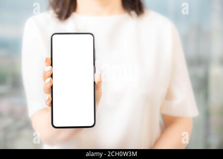 woman in white dress showing blank screen mobile phone Women hand show the mobile phone at the white screen, mockup Stock Photo