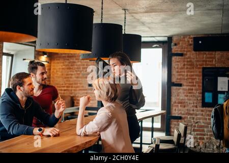 Cheerful group of students friends couple having fun arm wrestling each other in fashionable pub. Stock Photo