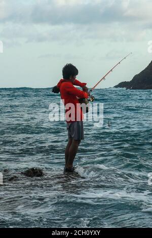 A local man in catches fish in the ocean on a sunny day to cook it for  lunch. Indonesian man in red hoodie catches fish on a fishing rod. A  fisherman Stock Photo - Alamy
