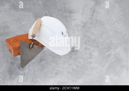 Bricklayer tools. Mason tools - Trowel, bricks and white helmet isolated on cement background, copyspace Stock Photo