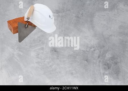 Bricklayer tools. Mason tools - Trowel, bricks and white helmet isolated on cement background, copyspace Stock Photo