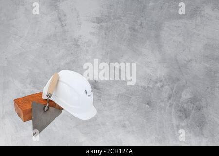 Construction set. Brick, white hard hat and Trowel on cement background. construction concept Stock Photo