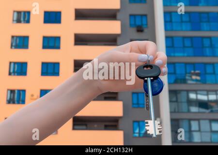 The hand of a white woman holds the keys on the background of new building. close up. real estate concept Stock Photo