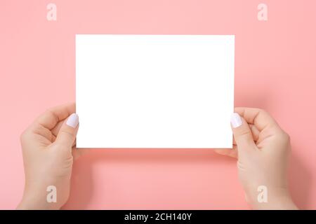 Women's hands holding a blank paper sheet, on pink. Mockup of a empty sheet of paper Stock Photo
