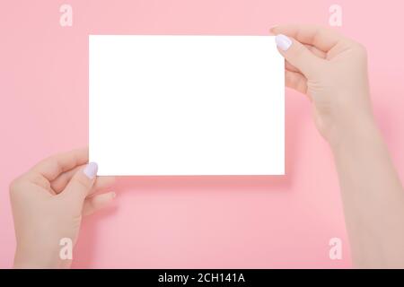 Women's hands holding a blank paper sheet, on pink. Mockup of a empty sheet of paper Stock Photo